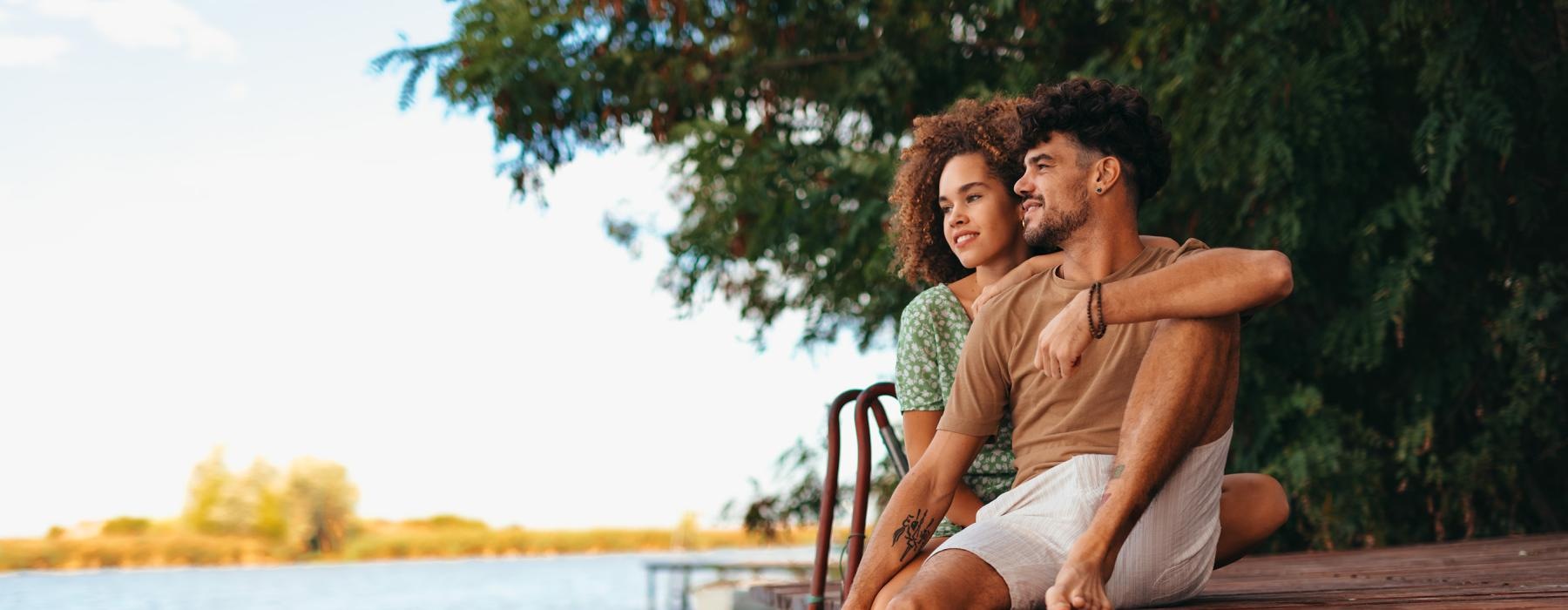 a man and a woman sitting on a dock by a body of water